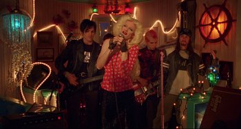 Movie still from “Hedwig and the Angry Inch” (2001), directed by John Cameron Mitchell – A group of young people standing in a room with lights; Wide shot, Over the shoulder angle
