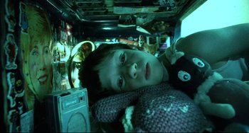 Movie still from “Hedwig and the Angry Inch” (2001), directed by John Cameron Mitchell – A young boy laying down in a room with electronics; Close Up shot, Overhead angle