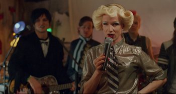 Movie still from “Hedwig and the Angry Inch” (2001), directed by John Cameron Mitchell – A man with blonde hair is holding a microphone; Close Up shot, Over the shoulder angle