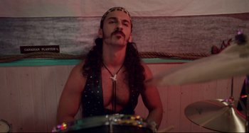 Movie still from “Hedwig and the Angry Inch” (2001), directed by John Cameron Mitchell – A man with long curly hair and a beard is playing drums; Medium shot, Over the shoulder angle