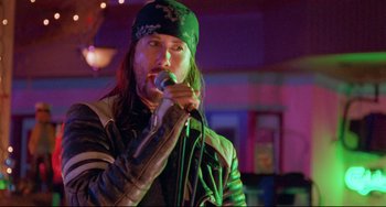 Movie still from “Hedwig and the Angry Inch” (2001), directed by John Cameron Mitchell – A man with long black hair wearing a black hat is holding a microphone; Close Up shot, Low angle