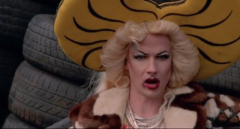 Movie still from “Hedwig and the Angry Inch” (2001), directed by John Cameron Mitchell – A drag queen wearing a yellow hat and a fur coat; Close Up shot, Overhead angle