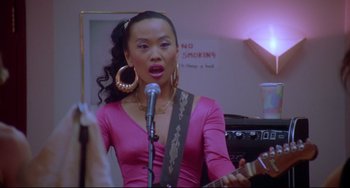 Movie still from “Hedwig and the Angry Inch” (2001), directed by John Cameron Mitchell – A woman in a pink shirt is playing a guitar; Close Up shot, Over the shoulder angle