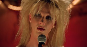 Movie still from “Hedwig and the Angry Inch” (2001), directed by John Cameron Mitchell – A woman with blonde hair holding a microphone; Close Up shot, Overhead angle