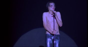 Movie still from “Hedwig and the Angry Inch” (2001), directed by John Cameron Mitchell – A shirtless man holding a microphone on a stage; Medium shot, Low angle