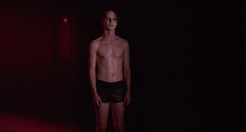 Movie still from “Hedwig and the Angry Inch” (2001), directed by John Cameron Mitchell – A man standing in the dark wearing black shorts; Medium shot, Low angle