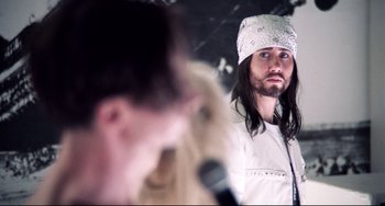 Movie still from “Hedwig and the Angry Inch” (2001), directed by John Cameron Mitchell – A man with long black hair and a white hat; Close Up shot, Over the shoulder angle