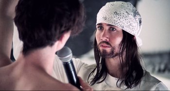 Movie still from “Hedwig and the Angry Inch” (2001), directed by John Cameron Mitchell – A man with long hair is holding a microphone; Close Up shot, Over the shoulder angle