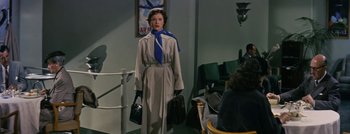 Movie still from “Hell and High Water” (1954), directed by Samuel Fuller – A woman wearing a trench coat and holding a purse; Medium shot, Low angle