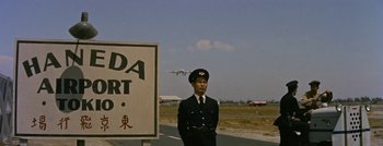 Movie still from “Hell and High Water” (1954), directed by Samuel Fuller – A man in a uniform standing in front of an airport sign; Extreme Wide shot, Low angle