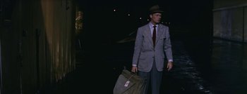 Movie still from “Hell and High Water” (1954), directed by Samuel Fuller – A man in a suit and hat holding a suitcase; Medium shot, Over the shoulder angle