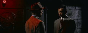 Movie still from “Hell and High Water” (1954), directed by Samuel Fuller – A man in a suit and a hat talking to another man in a suit and a hat; Medium shot, Over the shoulder angle