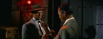 Movie still from “Hell and High Water” (1954), directed by Samuel Fuller – A man in a suit and a hat is holding a book; Close Up shot, Over the shoulder angle