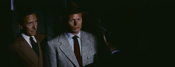Movie still from “Hell and High Water” (1954), directed by Samuel Fuller – A man wearing a suit and a hat is talking to another man in a suit; Close Up shot, Over the shoulder angle