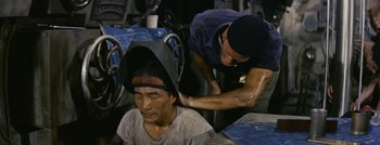 Movie still from “Hell and High Water” (1954), directed by Samuel Fuller – A man is getting his head shaved by a man with a helmet on; Medium shot, High angle