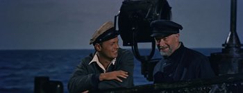 Movie still from “Hell and High Water” (1954), directed by Samuel Fuller – A man in a cap and a hat sitting next to another man in a hat; Medium shot, Over the shoulder angle