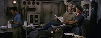 Movie still from “Hell and High Water” (1954), directed by Samuel Fuller – An older man sitting on the floor reading a newspaper; Medium shot, High angle