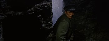 Movie still from “Hell and High Water” (1954), directed by Samuel Fuller – A man wearing a hat standing next to a rock wall; Medium shot, High angle