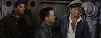 Movie still from “Hell and High Water” (1954), directed by Samuel Fuller – A man standing next to another man in front of a fire place; Medium shot, Over the shoulder angle