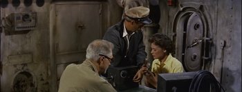 Movie still from “Hell and High Water” (1954), directed by Samuel Fuller – An older man and two young men looking at something on a phone; Medium shot, High angle