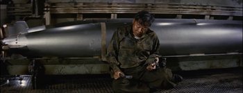 Movie still from “Hell and High Water” (1954), directed by Samuel Fuller – A man sitting on the ground holding a pair of scissors; Medium shot, High angle