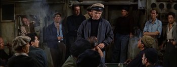 Movie still from “Hell and High Water” (1954), directed by Samuel Fuller – A group of people standing around a man with a hat on; Medium shot, High angle