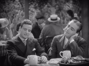 Movie still from “Hell's Angels” (1930), directed by Edmund Goulding – A couple of men sitting at a table with a cup; Medium shot, High angle
