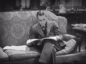 Movie still from “Hell's Angels” (1930), directed by Edmund Goulding – A black and white photo of a man sitting on a couch reading; Medium shot, High angle