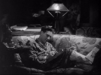 Movie still from “Hell's Angels” (1930), directed by Edmund Goulding – A man sitting on top of a couch reading a book; Medium shot, High angle