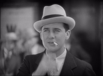 Movie still from “Hell's Angels” (1930), directed by Edmund Goulding – A black and white photo of a man in a suit and hat smoking a cigarette; Close Up shot, High angle