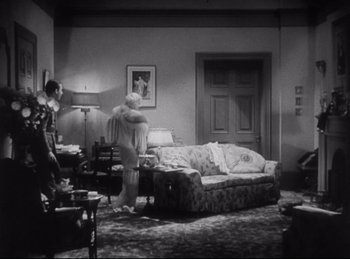 Movie still from “Hell's Angels” (1930), directed by Edmund Goulding – Two people in a living room with a couch and a table; Wide shot, High angle