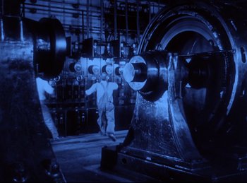Movie still from “Hell's Angels” (1930), directed by Edmund Goulding – A man standing next to a machine in a room; Wide shot, Low angle