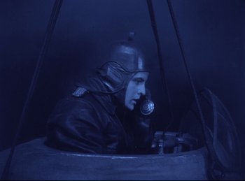 Movie still from “Hell's Angels” (1930), directed by Edmund Goulding – A man wearing a helmet and a gas mask in a tank; Medium shot, High angle