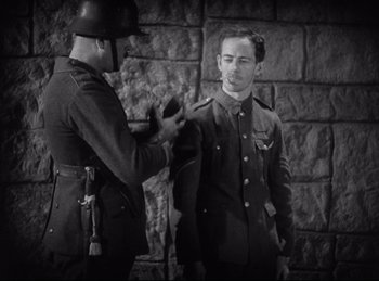 Movie still from “Hell's Angels” (1930), directed by Edmund Goulding – Two men in uniform are standing next to a stone wall; Medium shot, Low angle