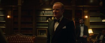 Movie still from “Hellboy” (2019), directed by Neil Marshall – A man in a tuxedo standing in front of a bookcase; Medium shot, Over the shoulder angle