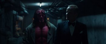 Movie still from “Hellboy” (2019), directed by Neil Marshall – A man in a suit standing next to another man in a suit; Medium shot, Over the shoulder angle