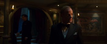 Movie still from “Hellboy” (2019), directed by Neil Marshall – A man in a tuxedo standing in front of a painting; Medium shot, Over the shoulder angle