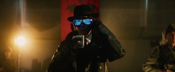 Movie still from “Hellboy” (2019), directed by Neil Marshall – A man in a hat and sunglasses holding a cell phone; Medium shot, Over the shoulder angle