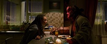 Movie still from “Hellboy” (2019), directed by Neil Marshall – Two people sitting at a dinner table , one of which has a red mask on his face; Medium shot, Over the shoulder angle