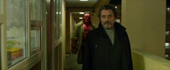Movie still from “Hellboy” (2019), directed by Neil Marshall – A man in a trench coat standing next to a man in a red mask; Medium shot, Over the shoulder angle