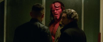 Movie still from “Hellboy” (2019), directed by Neil Marshall – A man with a red face is standing next to two other men; Medium shot, Over the shoulder angle