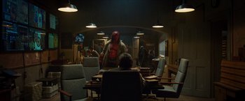 Movie still from “Hellboy” (2019), directed by Neil Marshall – A man in a red mask sitting at a table; Wide shot, Over the shoulder angle