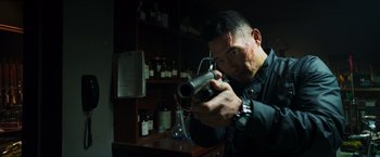 Movie still from “Hellboy” (2019), directed by Neil Marshall – A man holding a gun in a room with bottles on the wall; Close Up shot, Low angle