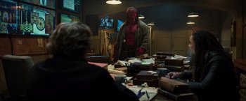 Movie still from “Hellboy” (2019), directed by Neil Marshall – A man with a red mask standing in front of a table; Wide shot, Over the shoulder angle