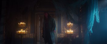 Movie still from “Hellboy” (2019), directed by Neil Marshall – A man in a green robe standing in front of candles in a room; Wide shot, High angle