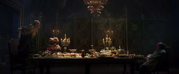 Movie still from “Hellboy” (2019), directed by Neil Marshall – A table filled with lots of food next to a chandelier; Wide shot, High angle