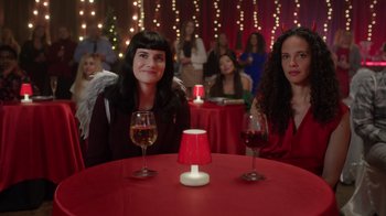 Movie still from “Under the Christmas Tree” (2021), directed by Lisa Rose Snow – Two women sitting at a table in front of a red lamp; Medium shot, Over the shoulder angle