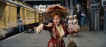 Movie still from “Hello, Dolly!” (1969), directed by Gene Kelly – A woman dressed in period costume and holding a purse; Medium shot, Low angle