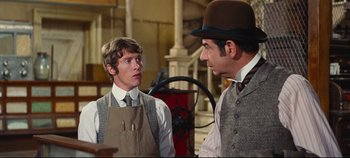Movie still from “Hello, Dolly!” (1969), directed by Gene Kelly – A man in an apron talking to another man in a hat; Medium shot, Over the shoulder angle