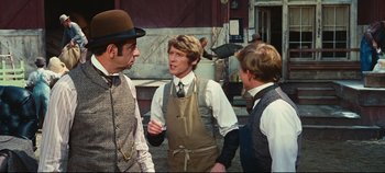 Movie still from “Hello, Dolly!” (1969), directed by Gene Kelly – A group of men standing next to each other on a street; Medium shot, Over the shoulder angle